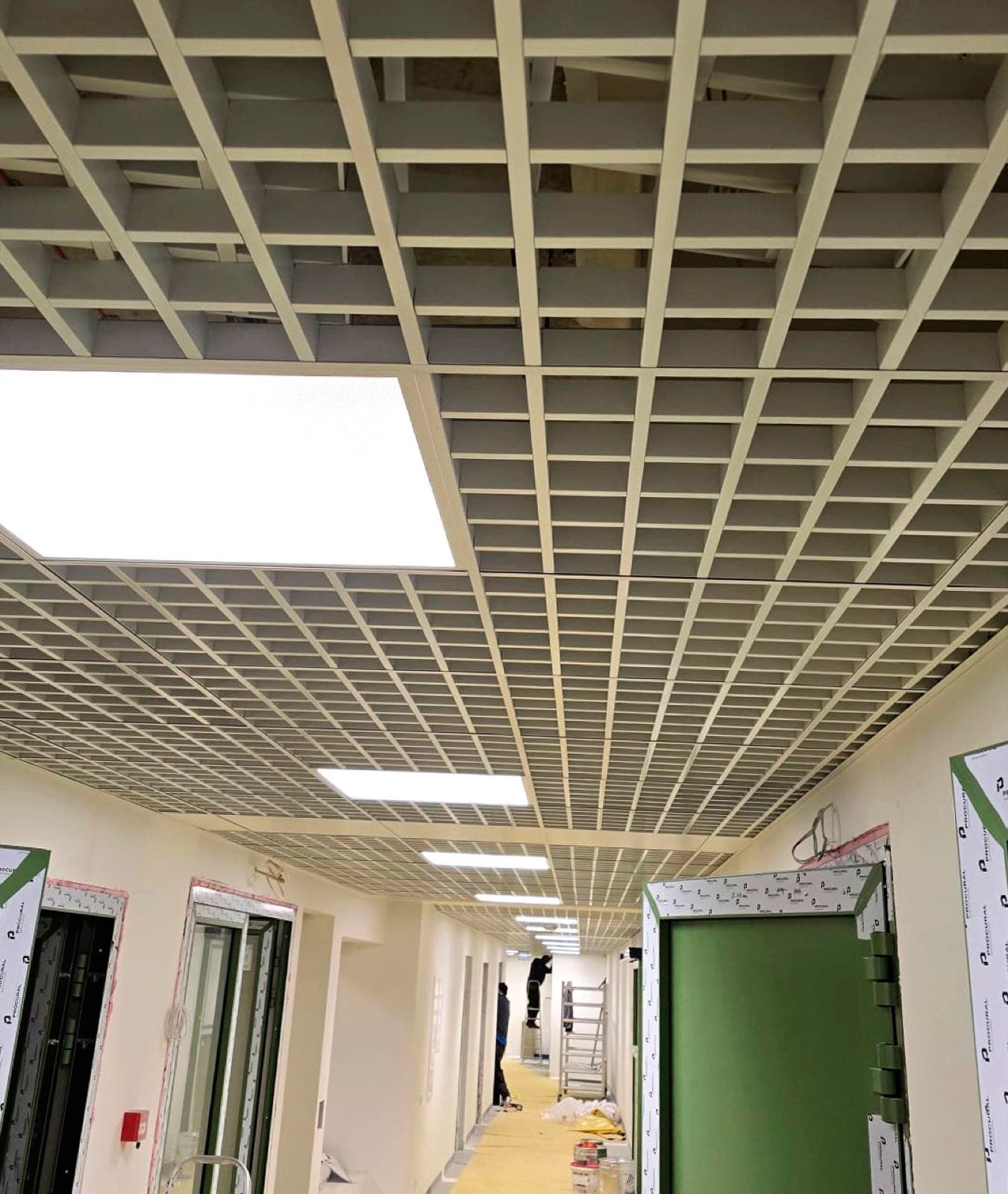 Atvērtā tipa režģa griesti koridorā ar iebūvētiem gaismas paneļiem