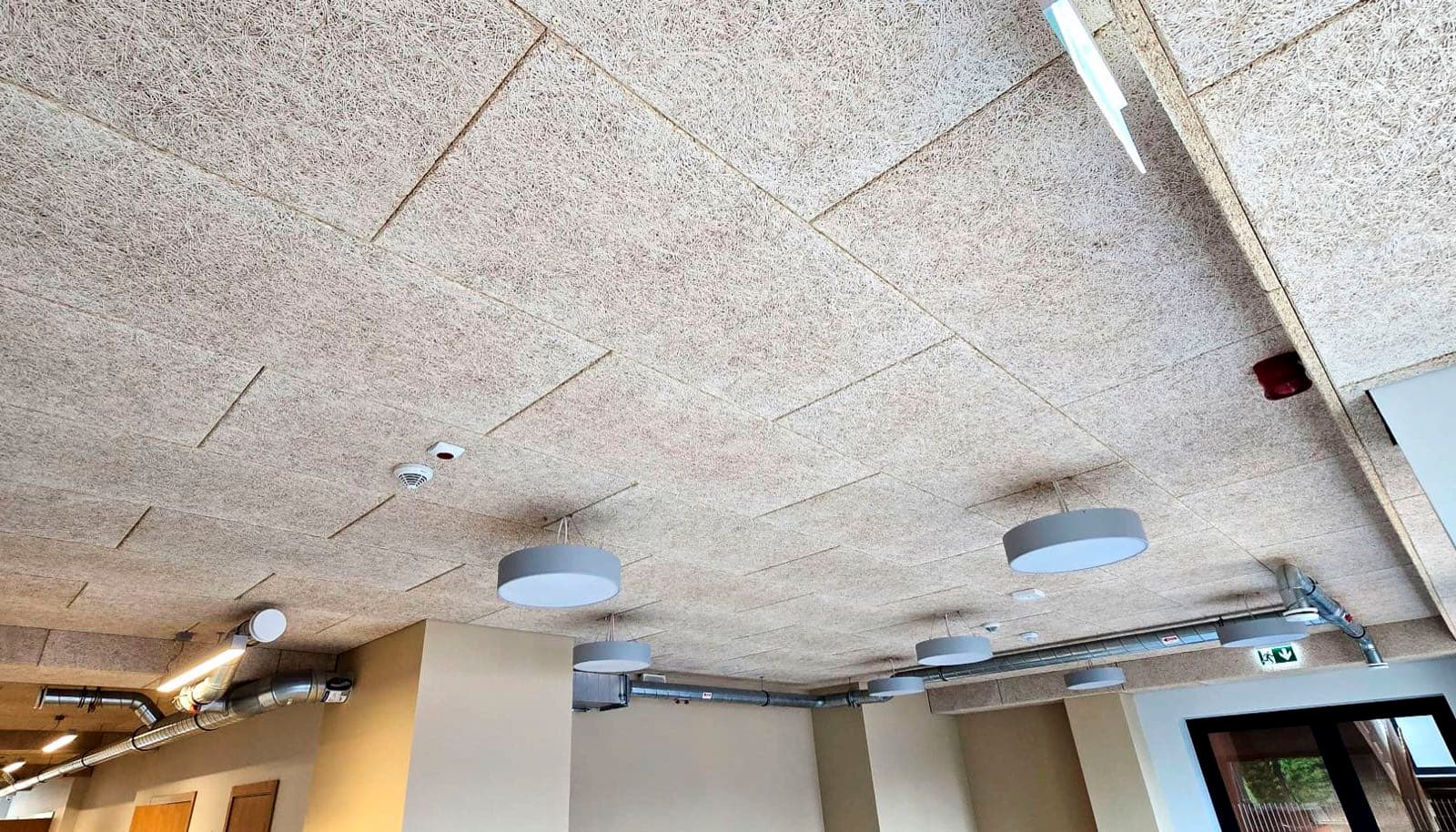 Plaša zāle ar koka skaidu griestiem, ventilācijas cauruļvadiem un apaļiem gaismekļiem